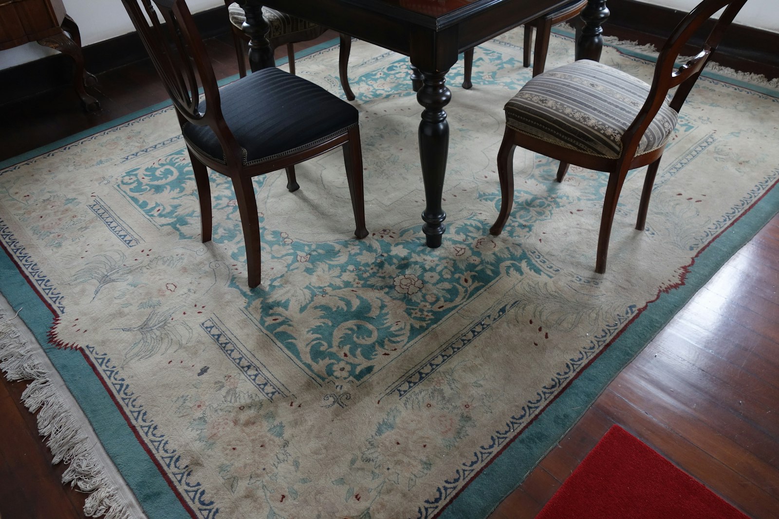 Ornate cream and teal patterned rug beneath a dark-wood dining table and antique chairs