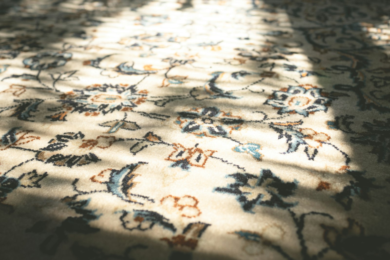 Close-up of a cream-based floral Persian carpet weave with dappled sunlight showing the knot texture