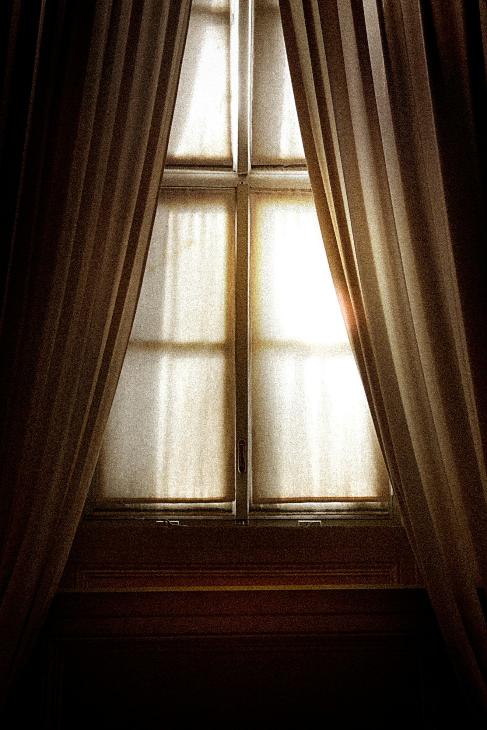 Heavy taupe floor-length curtains flanking a tall wood-framed window
