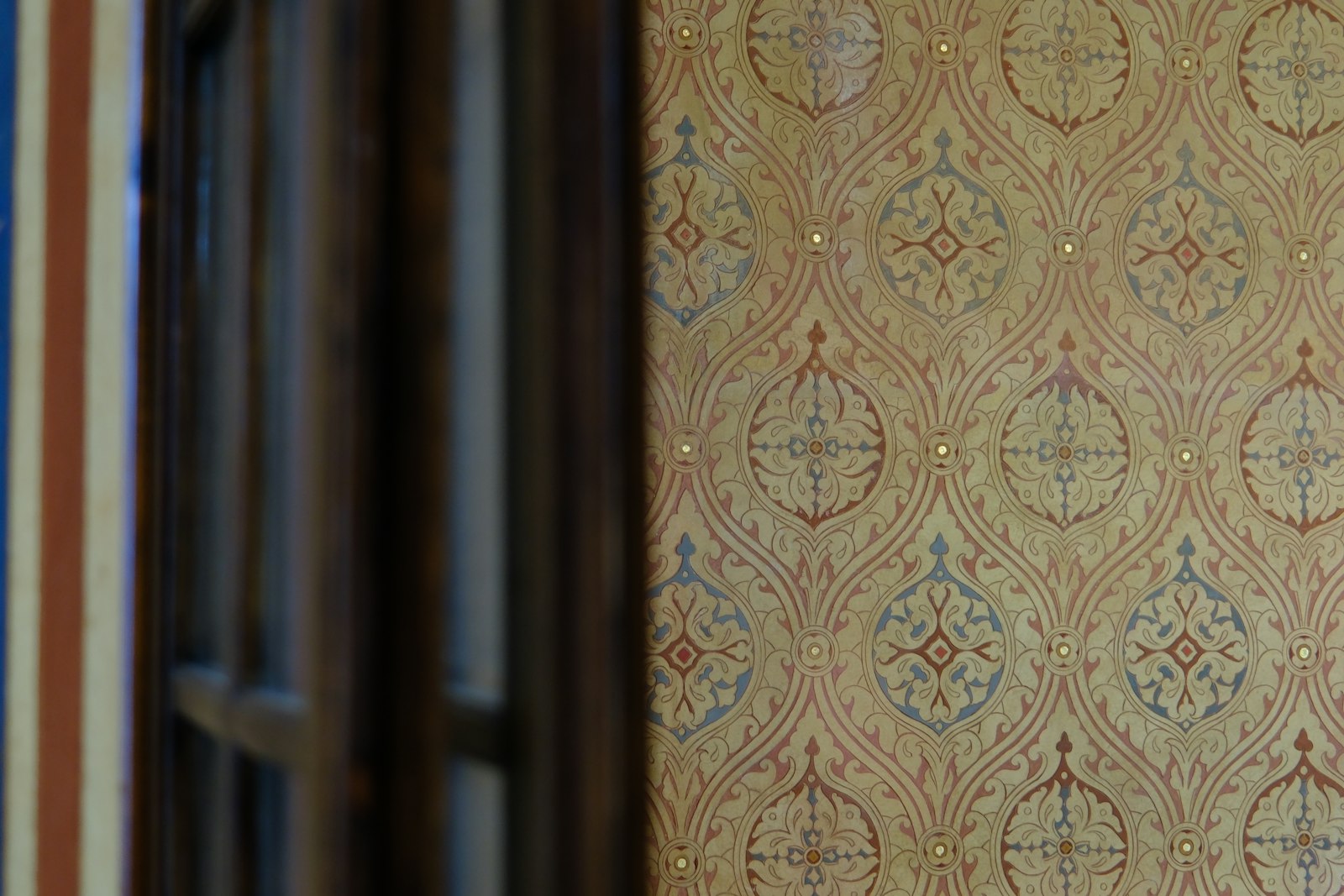 Warm gold and cream ornate ogee wallpaper with dark-wood window mullions in soft focus