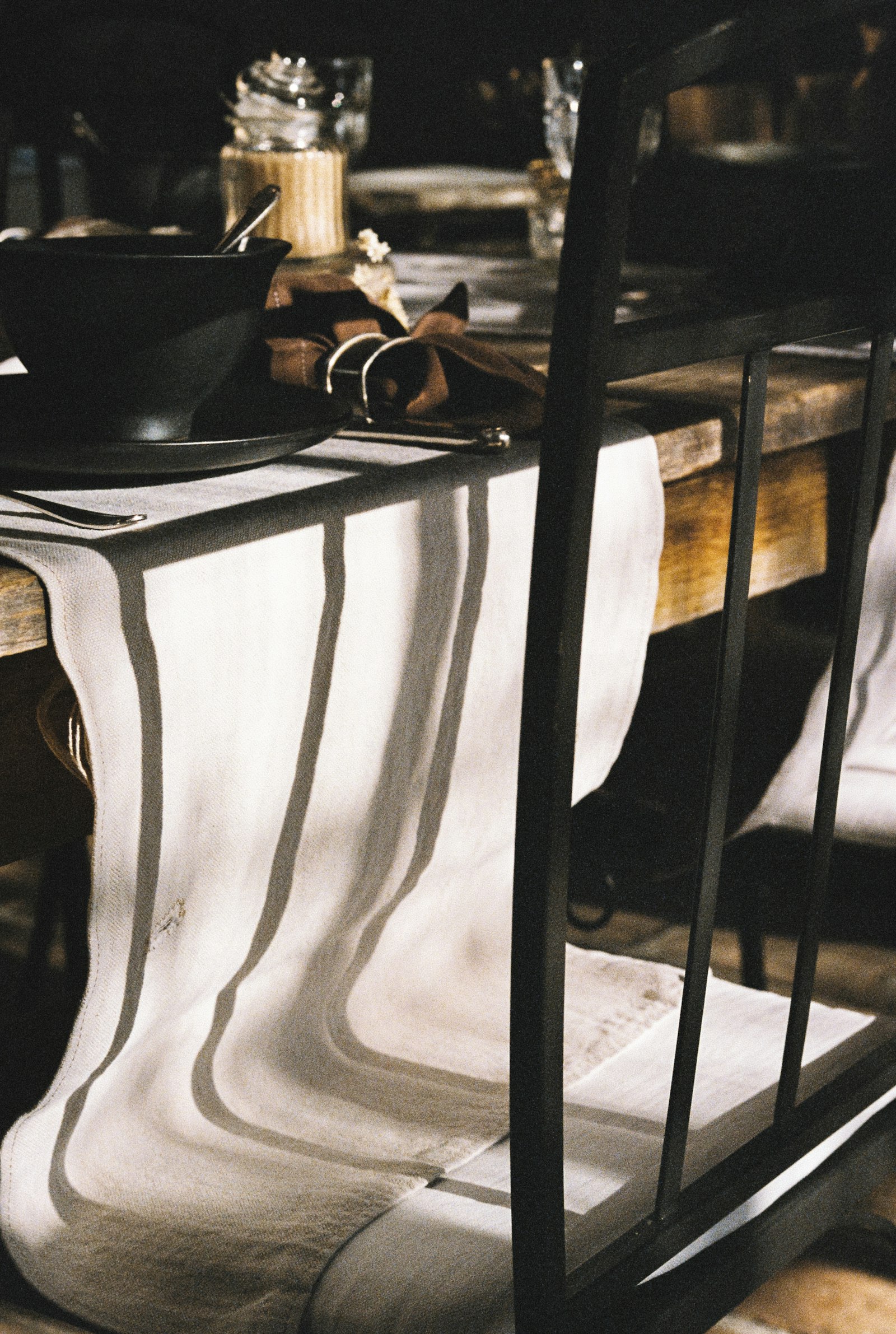 Striped linen runner draped across a dark-wood dining table, black stoneware bowl in frame