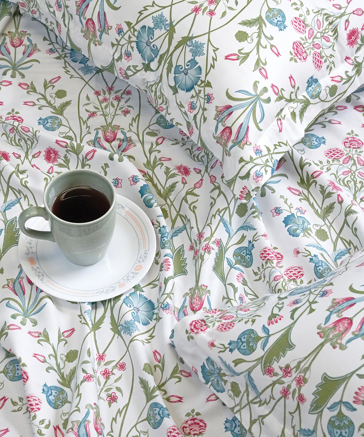 Close-up of a botanical-print cotton bedsheet with a coffee cup on a saucer